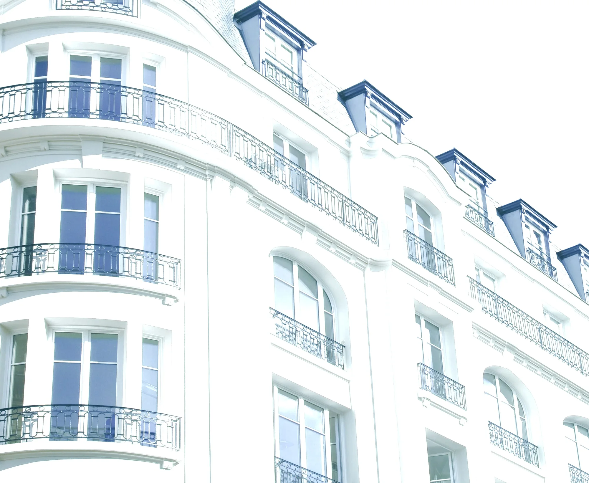 Façade haussmannienne claire en pierre, avec balcons en fer forgé et fenêtres à petits bois sur plusieurs étages.
